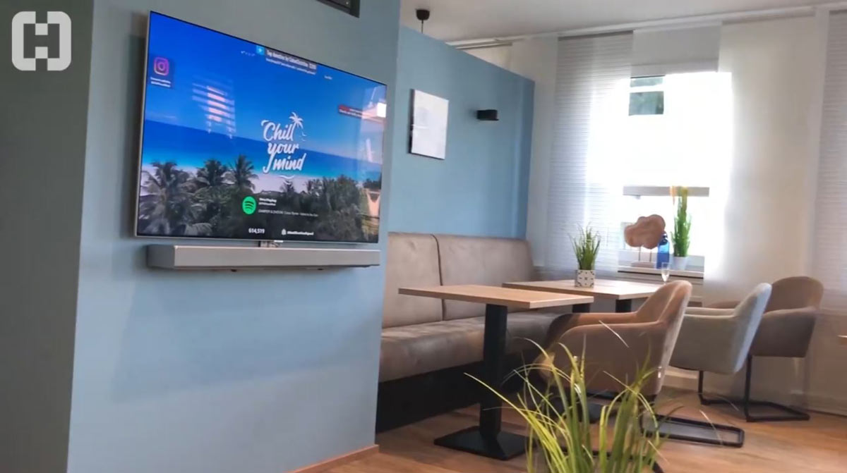 Einblick in die Business Lounge: ein TV an der Wand mit Tischen und Stühlen