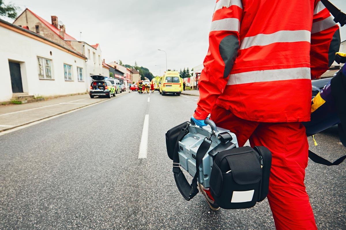 Sanitäter läuft mit Defibrillator zu einer Unfallstelle auf der Straße