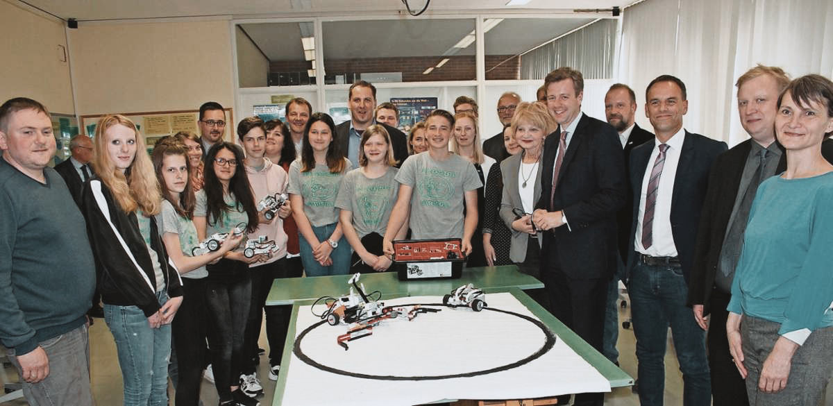 Gruppenbild Schüler und Lehrer – in der Mitte auf dem Tisch eine Art Kartbahn mit selbstgebauten Komponenten