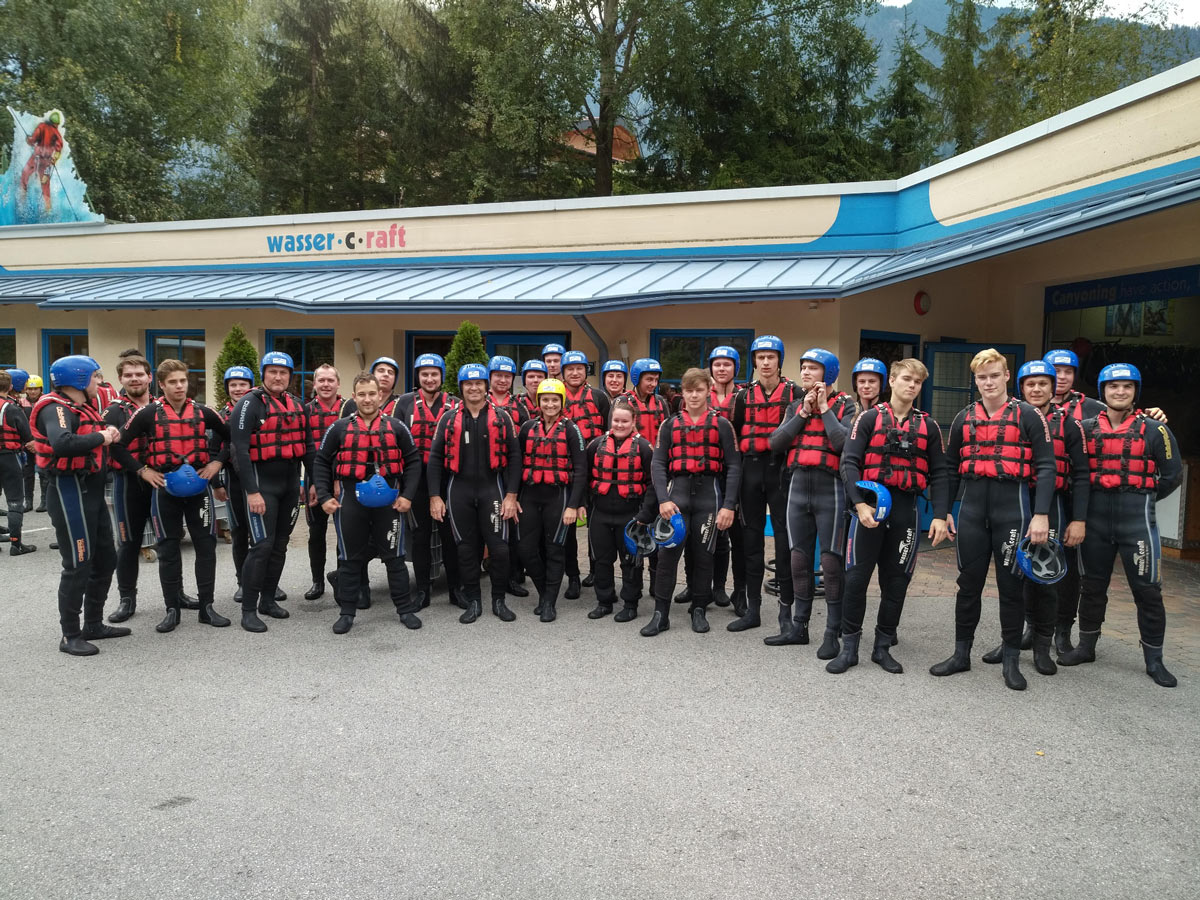 Gruppenfoto der Azubis – angezogen mit roten Schwimmwesten, blauen Helmen und Neoprenanzügen