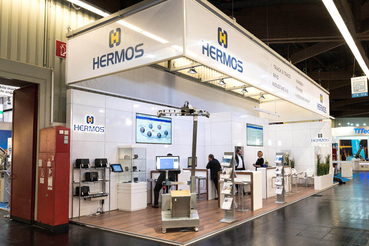 Der HERMOS-Messestand – weiße Seitenteile mit Logo und Laminatfußboden.