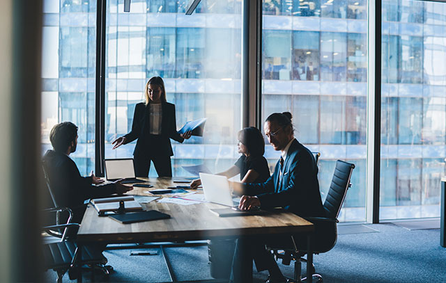 4 people sitting in a meeting room at a big table in front of a glass front