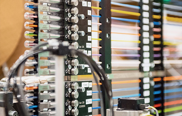 über zehn verschiedenfarbige Kabel horizontal übereinander in eine Maschine gespannt