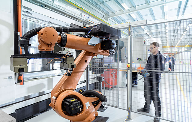 Ein orangenfarbiger Roboter in einem Käfig – dabei steht ein Mann, der ihn bedient
