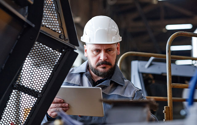 A man in blue overalls and a helmet performs quality control on a machine