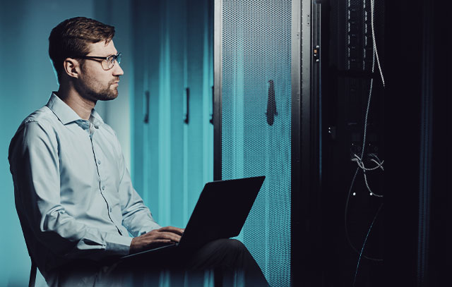 A service technician sits in front of a control cabinet with his laptop and works