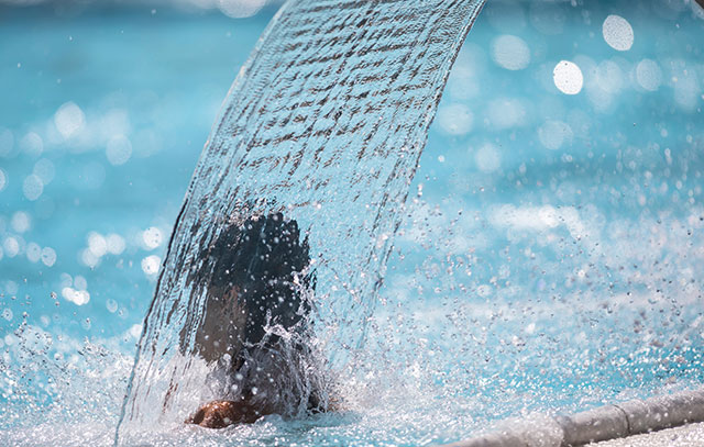 Eine Person ist im Schwimmbad und lässt sich von einem Wasserfall massieren