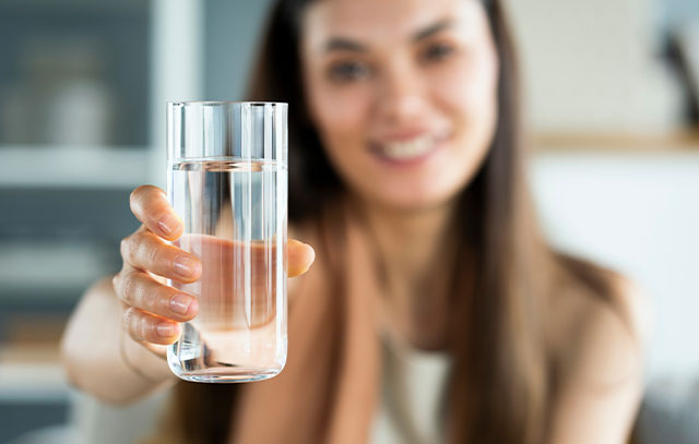 Frau hält ein Glas Wasser in die Kamera