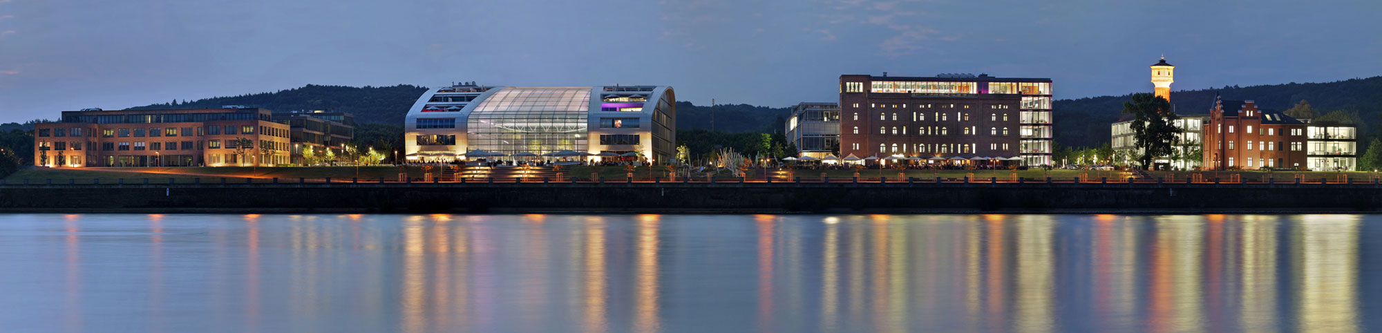 Eine Uferpromenade bei Nacht mit Blick auf verschiedene leuchtende Gebäude