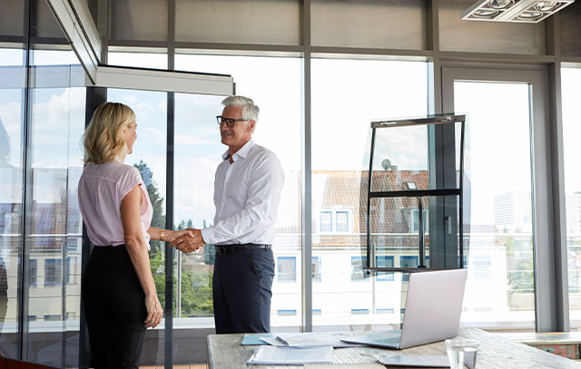 A gray haired man shakes hands with a blonde woman