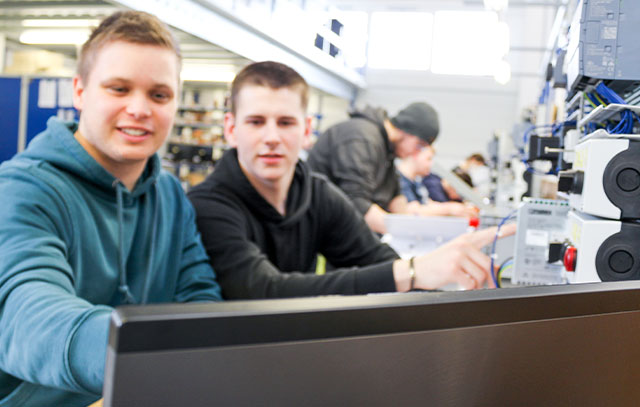 Two guys sitting at a workbench at a laptop