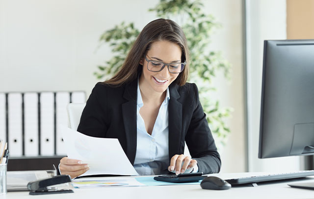 A woman sits at a desk and calculates with a calculator