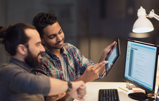 Two men with tablet in hand sitting in front of a computer