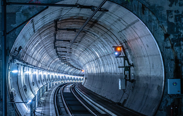 Blick in einen langen runden Tunnel mit Zugschienen und Beleuchtung an den Wänden