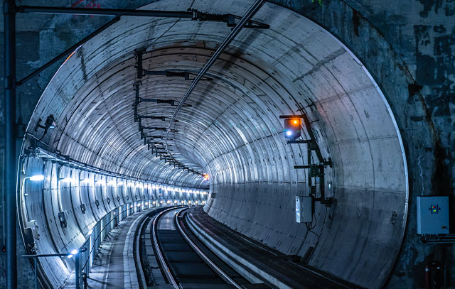 View into a long round tunnel with train tracks and lighting on the walls