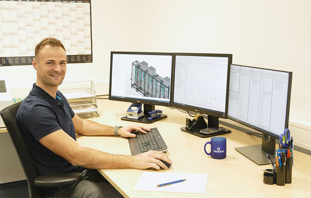 Ein Konstrukteur sitzt vor drei großen Bildschirmen an einem Schreibtisch