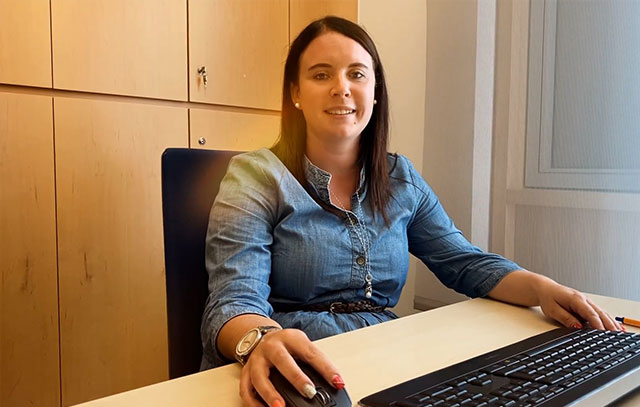 A woman sits at a desk and laughs into the camera