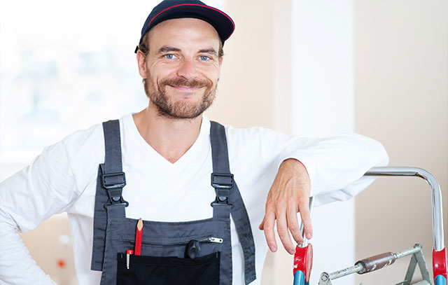 A man in work pants and cap smiles at the camera and leans against a Leister