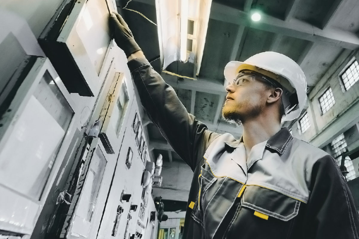 Ein Mann mit Schutzbrille und Helm bei der Arbeit an einem Schaltkasten